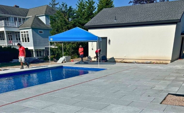 A pool with a blue tarp and umbrella, located on a stone deck in Stonington, CT, showcasing pool deck stone installation.