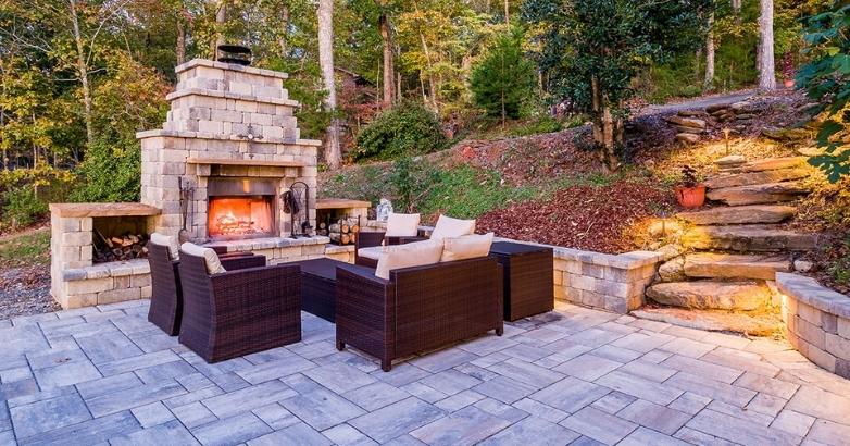 Paver patio with outdoor fireplace and seating area in landscaped backyard design