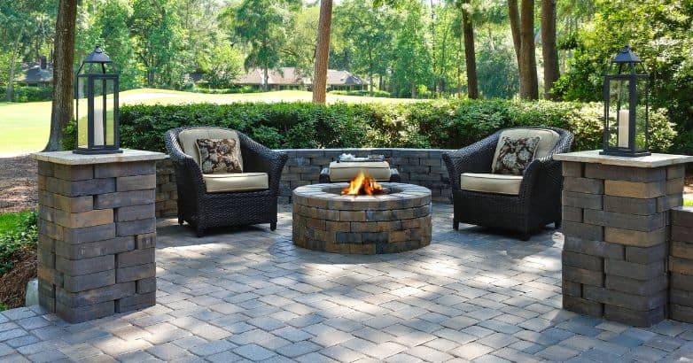 Durable paver patio with a built-in fire pit, outdoor seating, and stone columns in a landscaped backyard.
