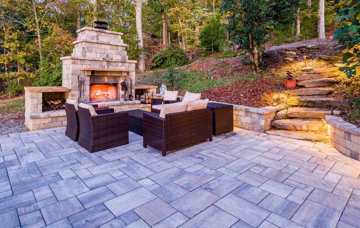 Custom paver patio with outdoor fireplace, retaining walls, and hillside seating area in Clinton CT
